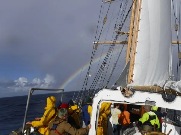 The author, Amelia, at the wheel about 100 nm off the North Cape of New Zealand AND The on-watch observed several full rainbows off the bow