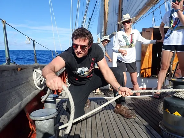 Steward Adam tactfully making fast (tying off the line) the main sheet, as (from right) Kerren, Carolyn, and Engineer JC look on in awe