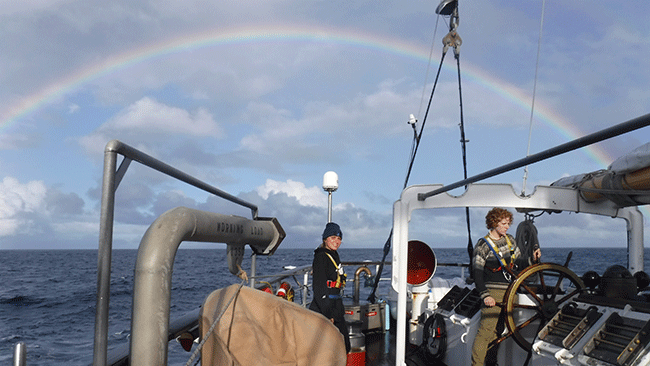 Lindsay on the quarterdeck with a full rainbow off the stern on the passage down to Wellington