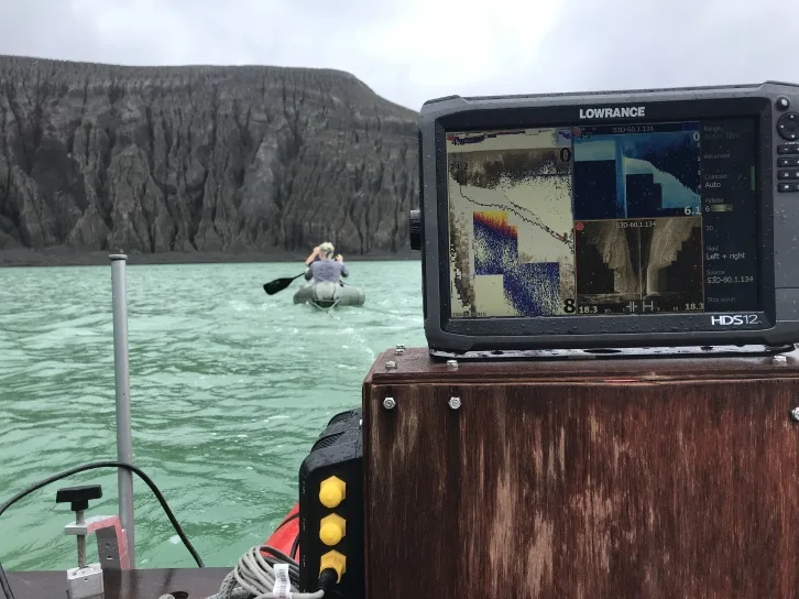 Collecting a side-scan sonar transect of the crater lake. The Lowrance is in the foreground, with Cam and Grace towing it in another inflatable raft. The crater wall is also in the background